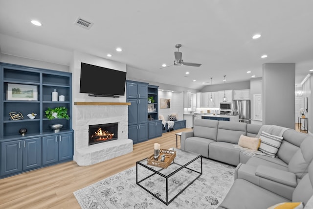 living area featuring ceiling fan, a stone fireplace, recessed lighting, visible vents, and light wood-style floors