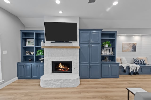 living area featuring recessed lighting, a stone fireplace, and light wood finished floors