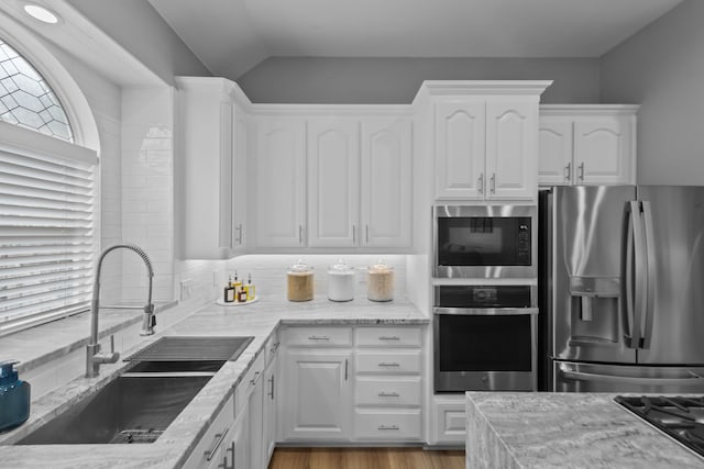 kitchen featuring stainless steel appliances, a sink, white cabinets, light stone countertops, and light wood finished floors