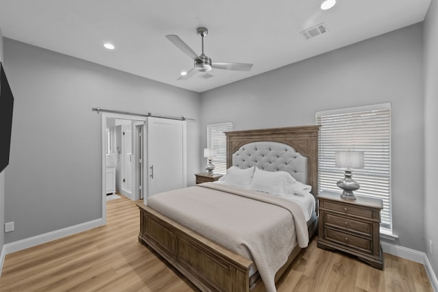 bedroom with a barn door, light wood-style flooring, visible vents, and baseboards