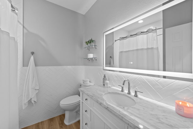 bathroom with toilet, a wainscoted wall, wood finished floors, vanity, and tile walls