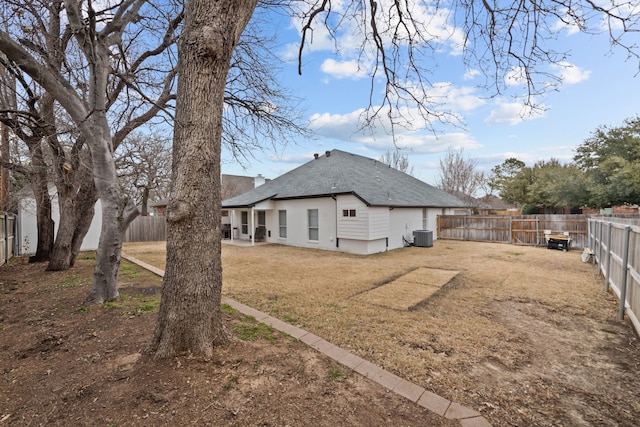 rear view of house with central air condition unit, a fenced backyard, and a yard