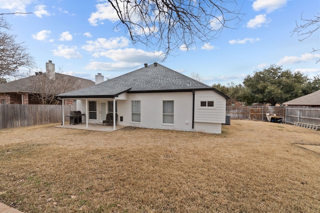 back of house featuring a yard, a fenced backyard, a shingled roof, and a patio