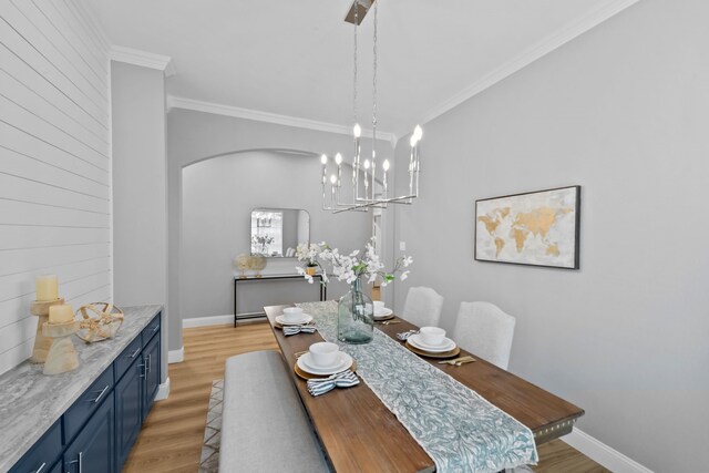 dining space featuring arched walkways, ornamental molding, light wood-style flooring, and baseboards