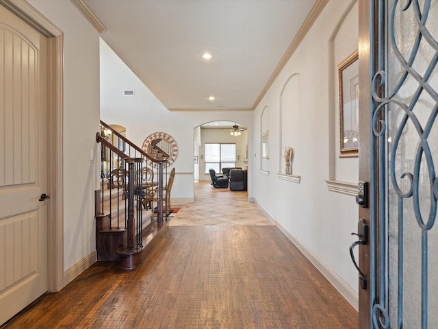 foyer entrance featuring arched walkways, wood finished floors, stairs, and crown molding