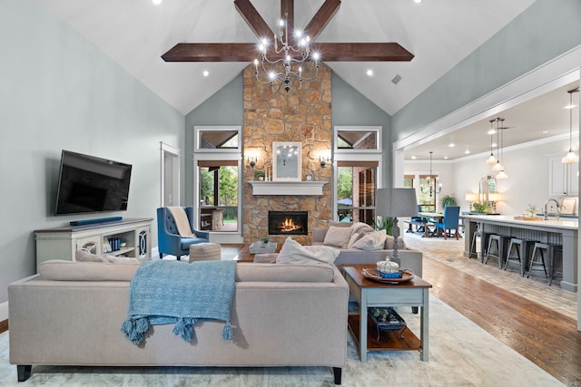 living room featuring high vaulted ceiling, a notable chandelier, a fireplace, light wood-style floors, and beam ceiling