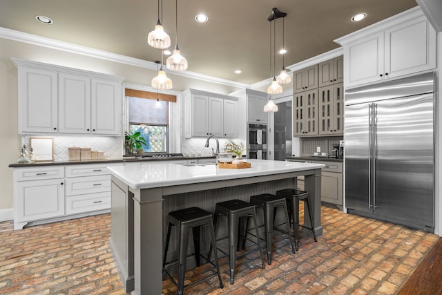 kitchen with glass insert cabinets, a breakfast bar area, a kitchen island with sink, stainless steel appliances, and crown molding