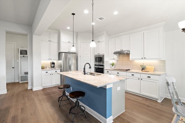 kitchen featuring light stone counters, a kitchen island with sink, stainless steel appliances, a sink, and white cabinets