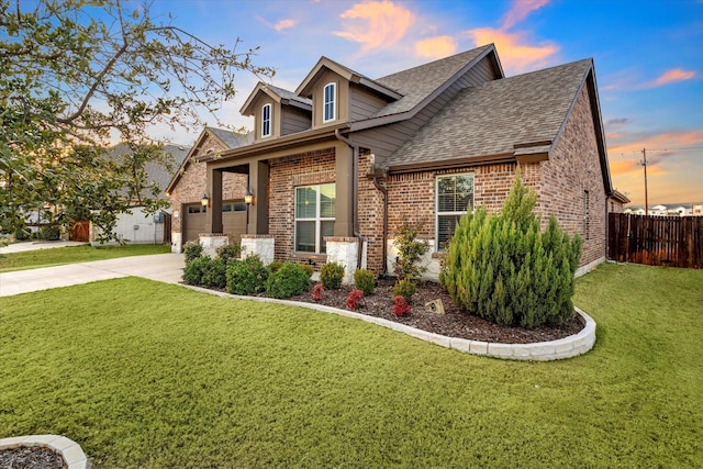 view of front facade with roof with shingles, brick siding, a lawn, fence, and driveway