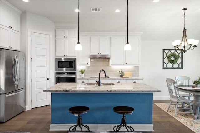 kitchen featuring hanging light fixtures, appliances with stainless steel finishes, a kitchen island with sink, and white cabinets