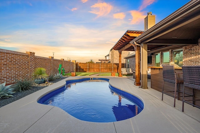 pool at dusk featuring a patio, a bar, a fenced backyard, and a fenced in pool