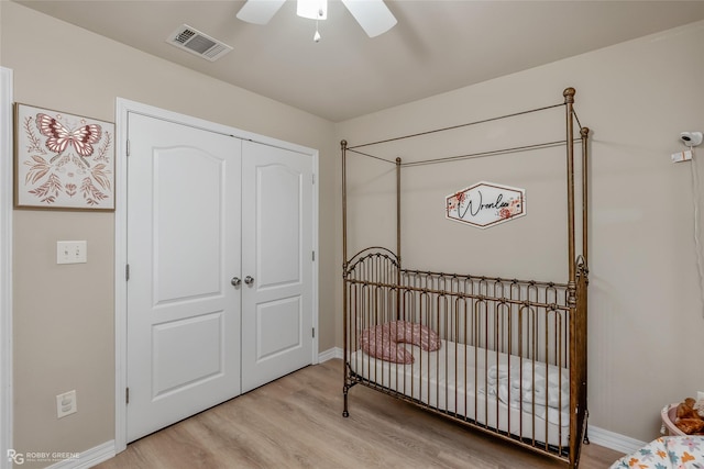 bedroom with a nursery area, a closet, visible vents, ceiling fan, and light wood-type flooring