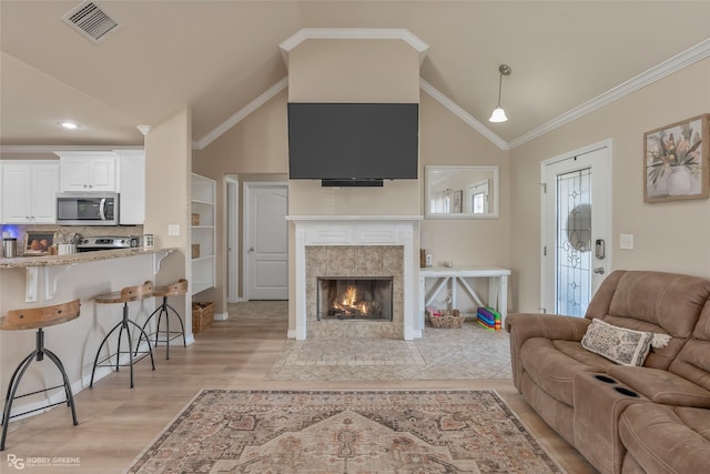 living area featuring light wood finished floors, visible vents, a tiled fireplace, lofted ceiling, and crown molding