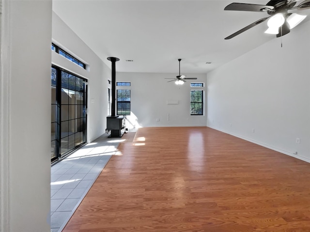 unfurnished living room featuring baseboards, ceiling fan, a wood stove, and light wood-style floors