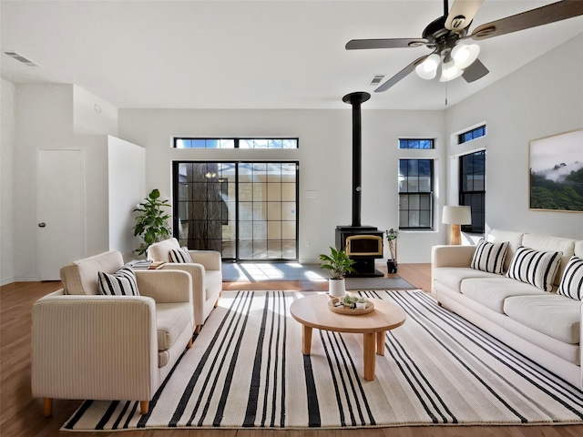 living room with ceiling fan, a wood stove, visible vents, and light wood-style floors