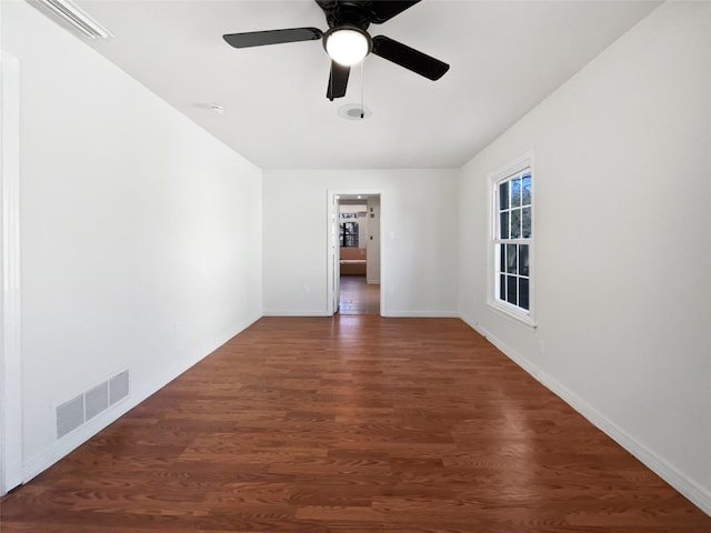 empty room featuring dark wood-type flooring, visible vents, and baseboards