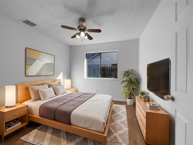 bedroom with dark wood-type flooring, visible vents, a textured ceiling, and a ceiling fan