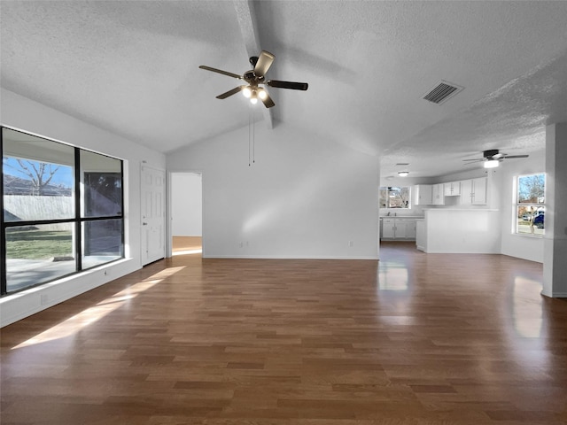 unfurnished living room with ceiling fan, a textured ceiling, visible vents, and dark wood-type flooring