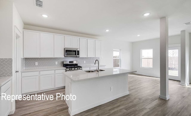 kitchen with white cabinets, an island with sink, appliances with stainless steel finishes, light countertops, and a sink