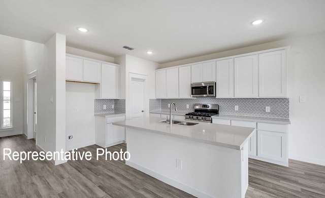 kitchen with light countertops, appliances with stainless steel finishes, a kitchen island with sink, and white cabinets