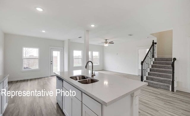 kitchen featuring dishwasher, an island with sink, open floor plan, light countertops, and a sink