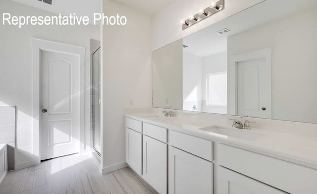 bathroom with a stall shower, visible vents, a sink, and double vanity