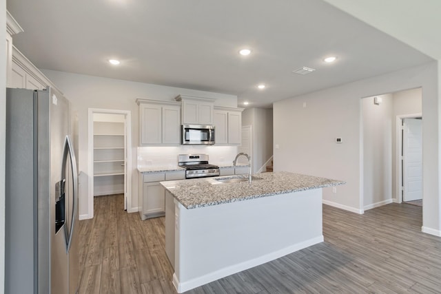 kitchen featuring light stone countertops, a kitchen island with sink, stainless steel appliances, white cabinetry, and a sink