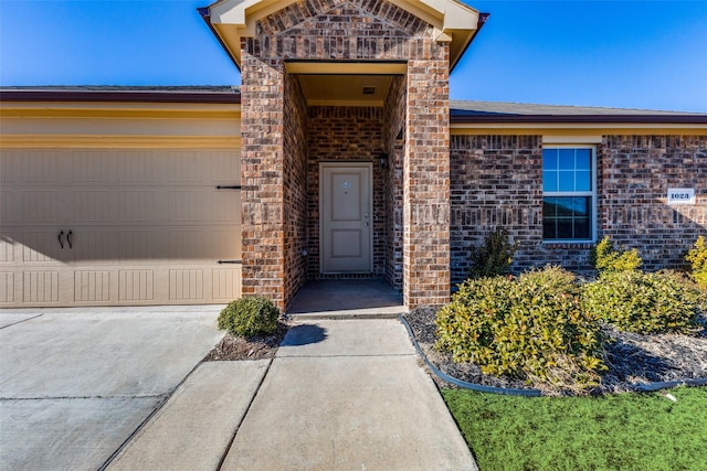 entrance to property featuring a garage, driveway, and brick siding