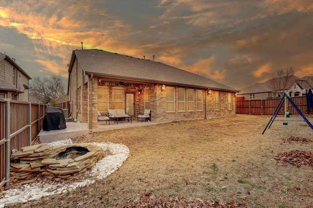 rear view of house featuring a patio, brick siding, a playground, and a fenced backyard