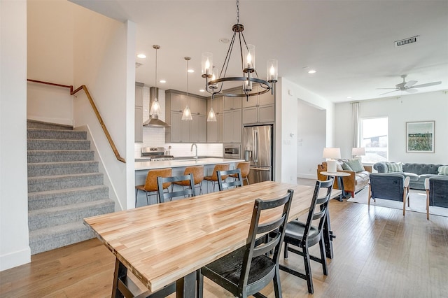 dining area with a ceiling fan, light wood-type flooring, visible vents, and stairway