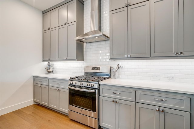 kitchen with gray cabinets, light countertops, light wood-style flooring, wall chimney range hood, and stainless steel gas range oven