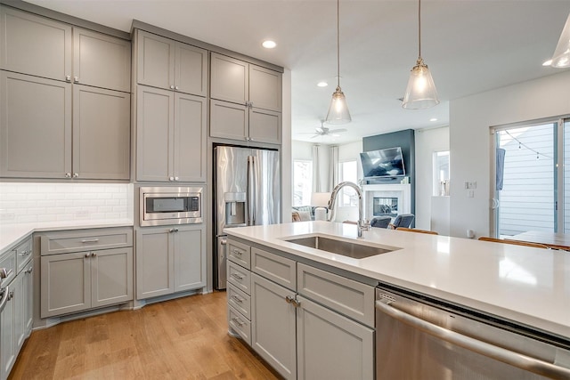 kitchen with light countertops, appliances with stainless steel finishes, a sink, and gray cabinetry