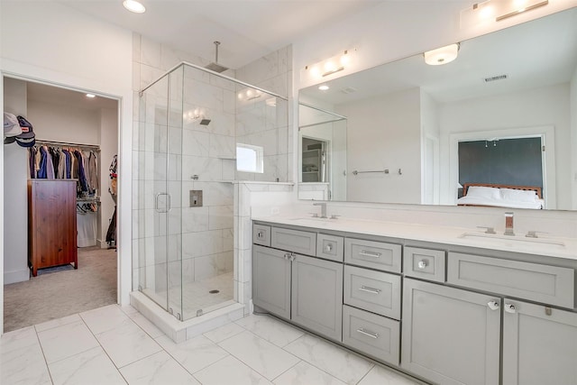 bathroom featuring double vanity, visible vents, a walk in closet, a shower stall, and a sink