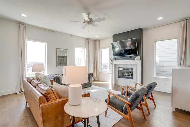 living area with baseboards, ceiling fan, a glass covered fireplace, and light wood-style floors