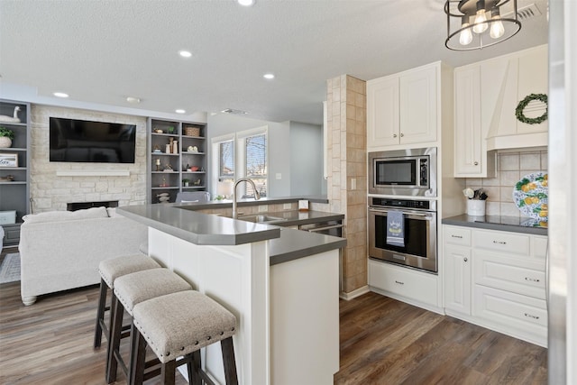 kitchen featuring appliances with stainless steel finishes, a fireplace, dark countertops, and a sink