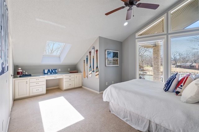 bedroom featuring a textured ceiling, built in desk, lofted ceiling with skylight, and light carpet