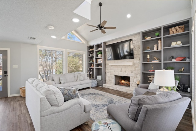 living room with a textured ceiling, a stone fireplace, wood finished floors, visible vents, and vaulted ceiling