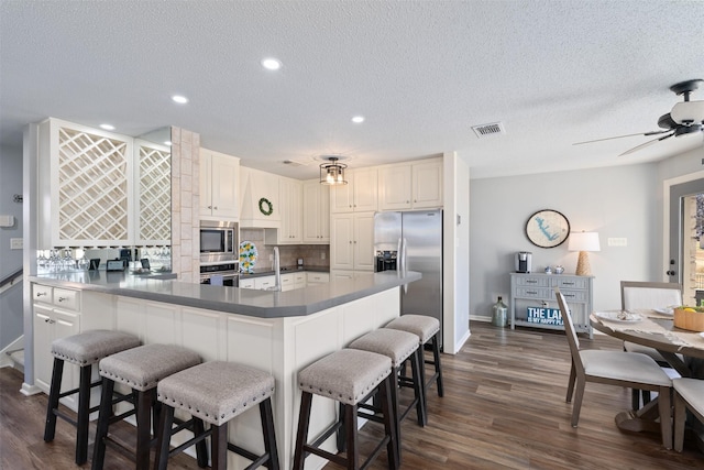 kitchen featuring a breakfast bar area, visible vents, appliances with stainless steel finishes, tasteful backsplash, and dark wood finished floors