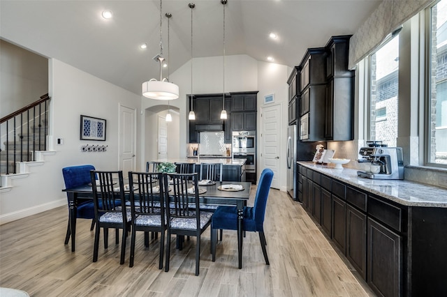 dining room featuring arched walkways, baseboards, light wood finished floors, and stairs