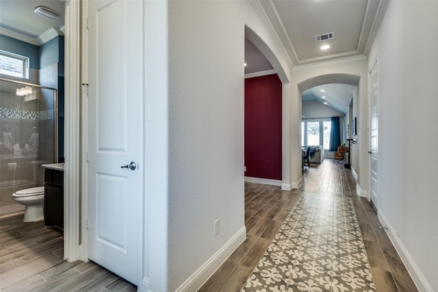 hallway featuring arched walkways, visible vents, baseboards, ornamental molding, and wood tiled floor