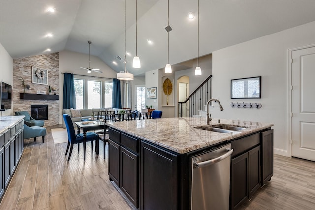 kitchen with stainless steel dishwasher, light wood-style floors, vaulted ceiling, a sink, and a stone fireplace