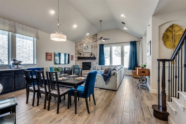 dining room with light wood-type flooring, stairs, and a stone fireplace