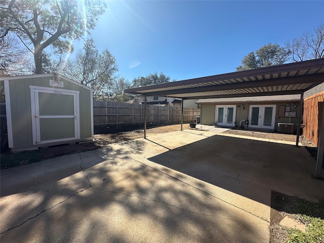 view of patio / terrace featuring driveway, french doors, fence, an outdoor structure, and a shed