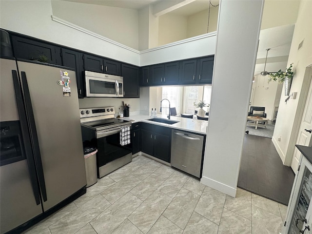 kitchen with a ceiling fan, dark cabinets, stainless steel appliances, light countertops, and a sink