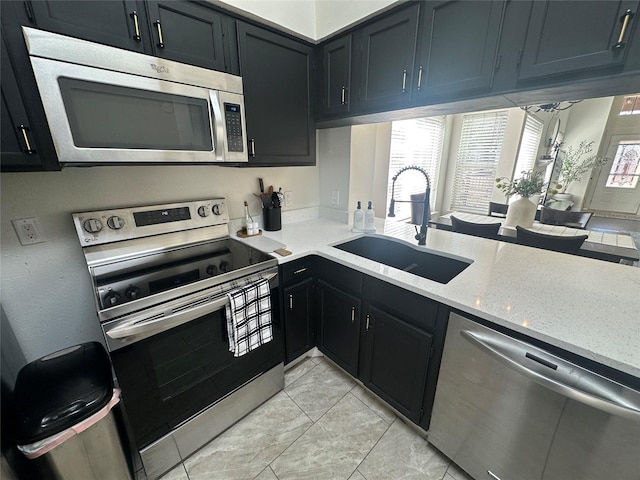 kitchen with stainless steel appliances, dark cabinetry, a sink, and light stone counters