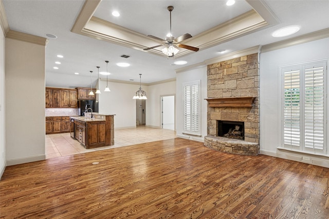 unfurnished living room with ceiling fan, light wood-style flooring, a fireplace, visible vents, and a raised ceiling