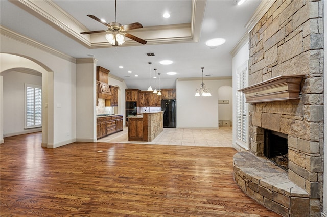 unfurnished living room with visible vents, arched walkways, a raised ceiling, ceiling fan, and a fireplace