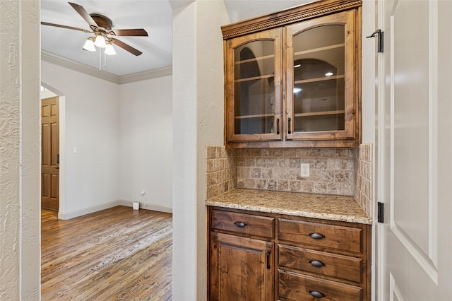 kitchen with baseboards, ornamental molding, light wood-type flooring, decorative backsplash, and glass insert cabinets