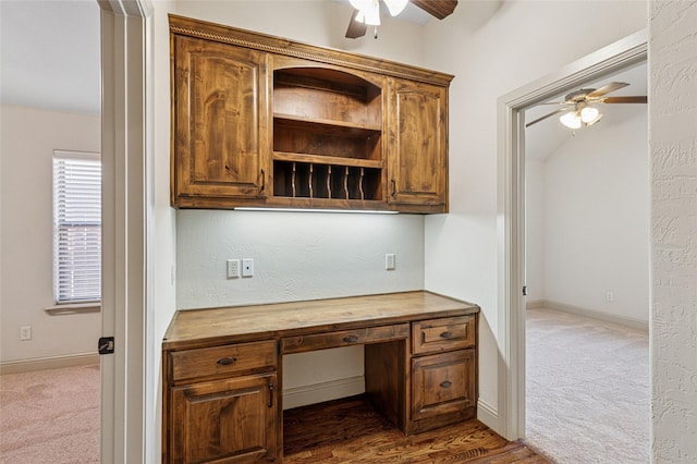 unfurnished office featuring built in desk, dark carpet, a ceiling fan, and baseboards