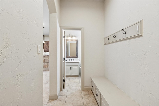 mudroom with a textured wall, a sink, and light tile patterned floors